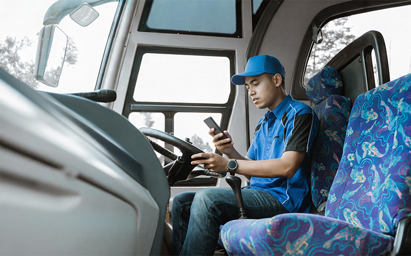 Bus driver using smartphone while seated at the wheel.